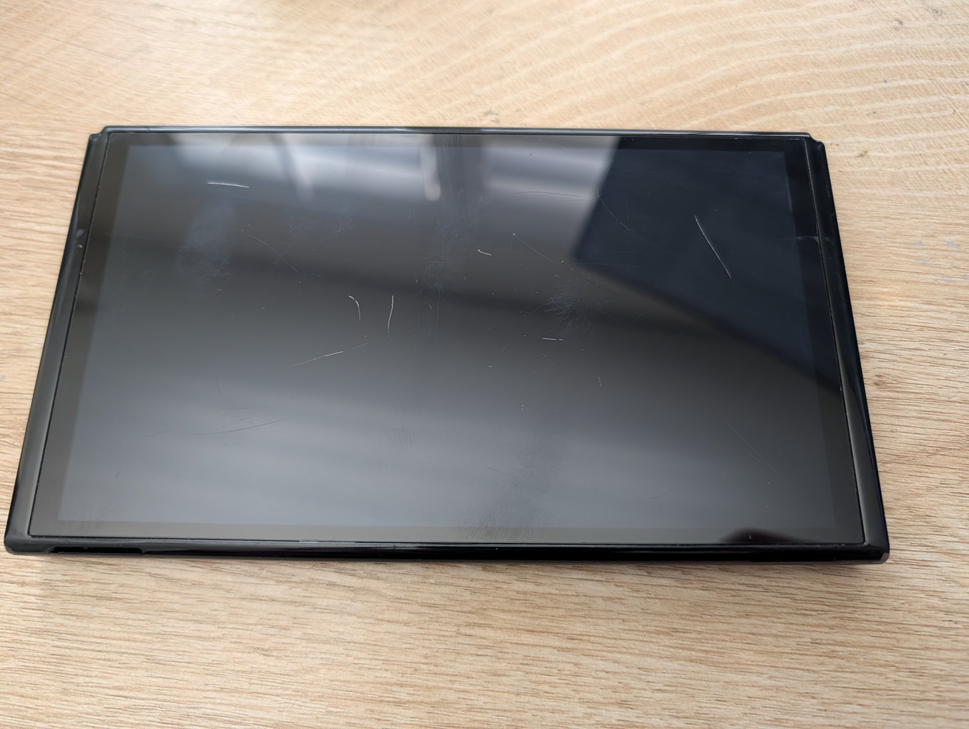 A black tablet or e-reader with a glossy screen, resting on a light-colored wooden surface.